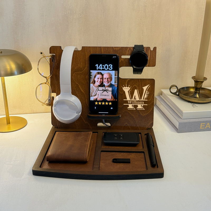 Brown wooden docking station with W initial engraving, holding a phone, headphones, watch and wallet